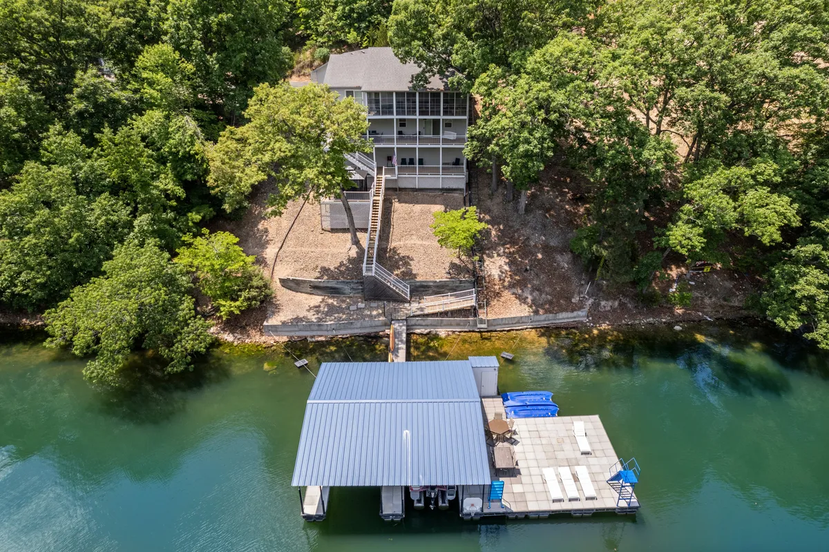 A tranquil view of the house nestled near the water’s edge, with a private dock extending into the lake and surrounded by lush greenery. The dock is central, inviting guests to imagine launching a boat, casting a fishing line, or simply enjoying peaceful moments beside the water.