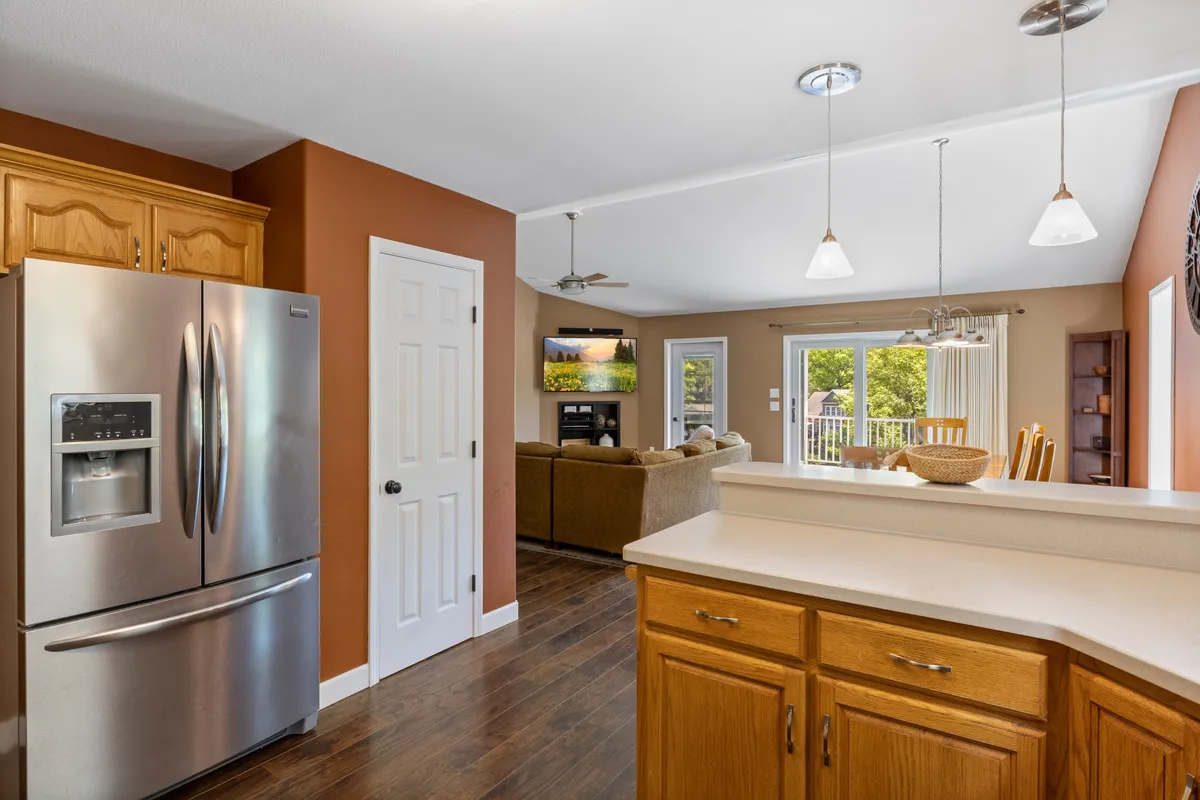 This image captures an open-concept living space that seamlessly combines the kitchen, dining, and living areas. The focal points include a stainless steel refrigerator, a central kitchen island perfect for meal prep or gathering, and large windows that bring in abundant natural light. The space looks warm and inviting, setting the scene for family gatherings and social moments.