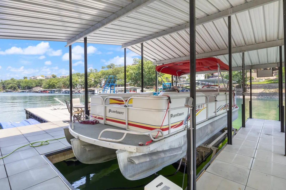 A pontoon boat sits at the dock, surrounded by tranquil water and lush trees. The setting is calm, perfect for boat rides, fishing, or simply soaking in the serene lakeside environment. The area is designed for both relaxation and recreation.