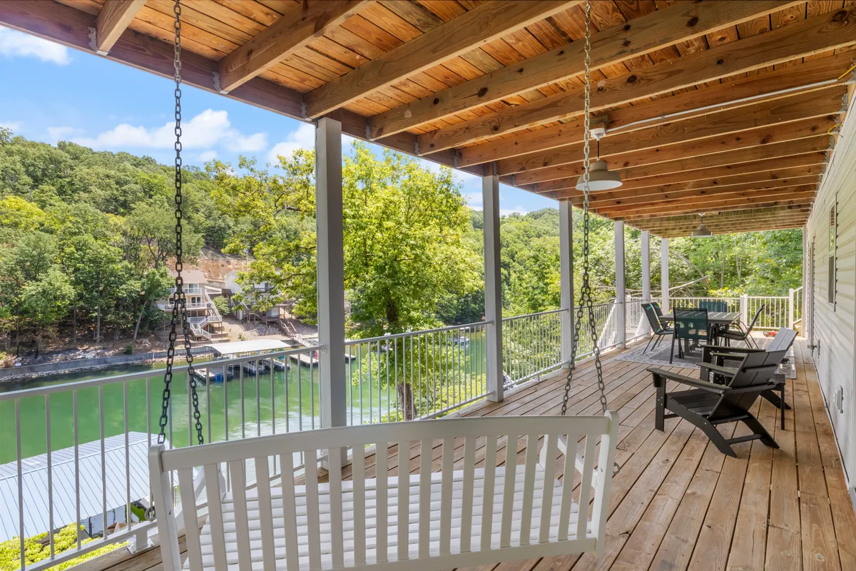 A peaceful lakeside area featuring a swing bench, Adirondack chairs, lush greenery, and tranquil water. The setting encourages relaxation, conversation, and enjoying the view—perfect for sharing moments across all seasons, whether for a summer sunrise or a crisp fall evening.