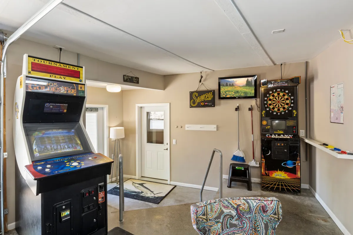 A cozy yet energetic corner of the game room displaying an arcade game machine, dartboard, television, and a colorful chair. The setting is ideal for family bonding during arcade tournaments, dart games, or relaxed TV time.