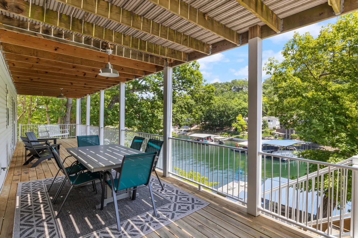 An inviting patio with a dining table overlooking a tranquil lake and surrounded by lush trees. The setting is perfect for outdoor relaxation or continuing the fun from the game room onto the patio, embracing the seamless indoor-outdoor flow suggested in the section.