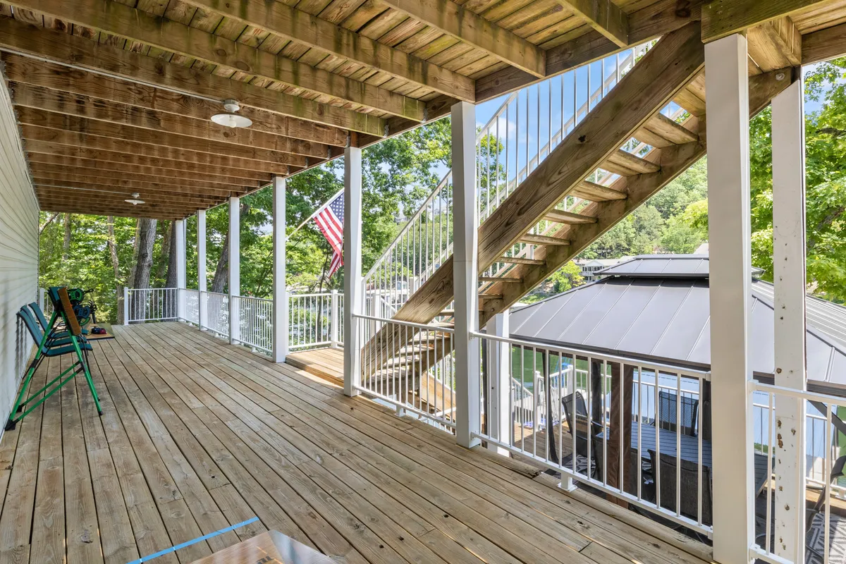 A wooden deck surrounded by trees, featuring a staircase and an American flag. The deck is set up for relaxing and socializing, and the natural environment enhances the sense of seasonal change and outdoor enjoyment.
