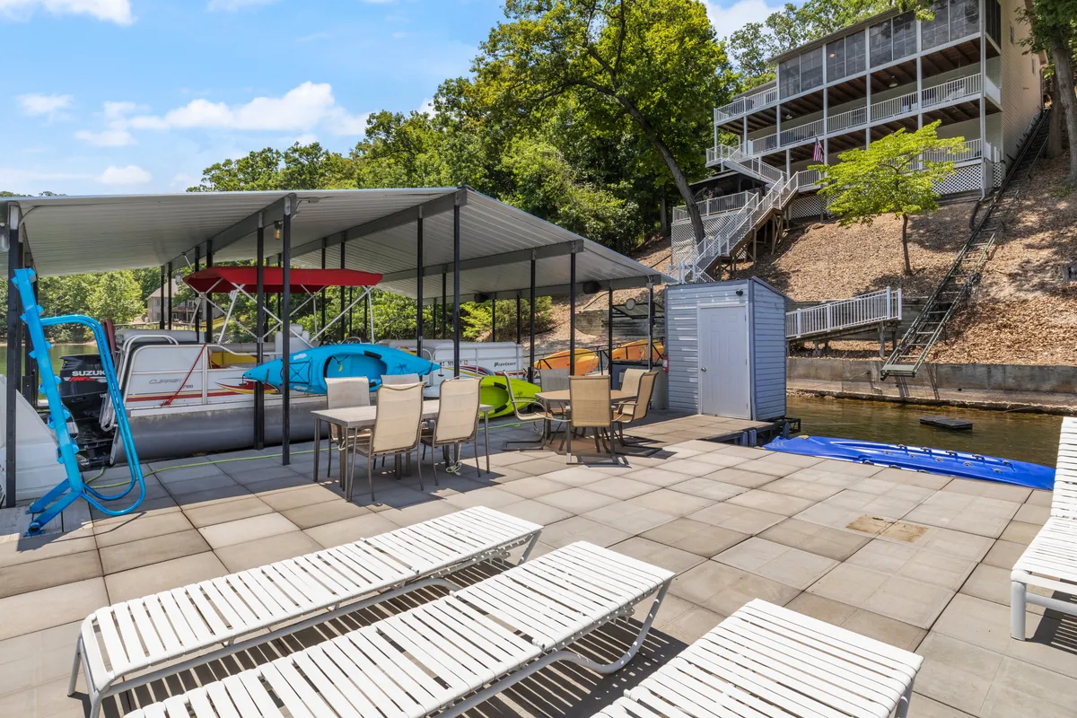 A waterfront dock with a covered boat slip, lounge chairs, a dining table, and kayaks ready for adventure. The setting is relaxed and offers direct access to the water, ideal for sunbathing, outdoor dining, or launching kayak trips.