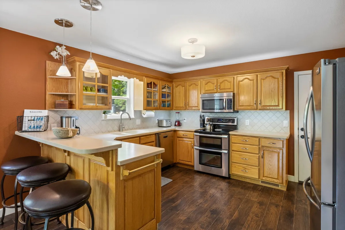 Featuring a spacious kitchen with a large island, stainless steel appliances, wooden cabinetry, and a window infusing the space with natural light, this image showcases a welcoming environment for cooking and casual dining. The layout suggests ample room for several people to prep, cook, or simply enjoy a coffee together.